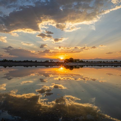 A picturesque sunset reflecting off the surface of a serene lake, with clouds overhead.