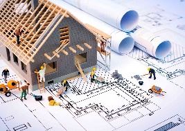 Model of a house under construction placed on top of architectural blueprints, with small figurines 