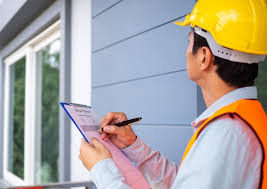 A building inspector in a yellow hard hat and orange safety vest holding a clipboard and pen