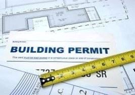 A building permit and a measuring tape placed on top of architectural blueprints.
