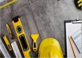 A construction workspace tools, including a yellow hard hat, level, measuring tape, and clipboard 