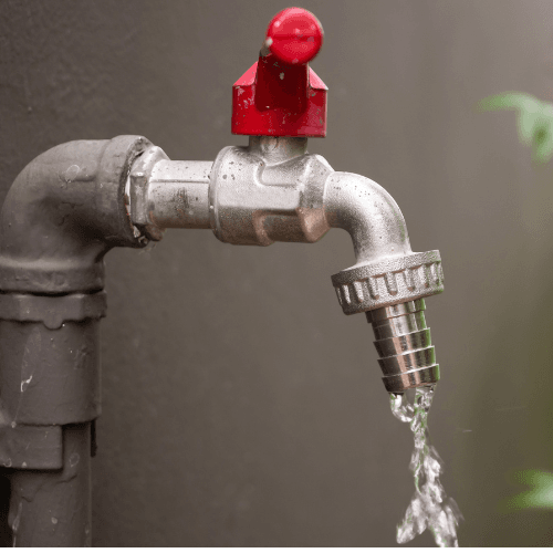 Water flowing from a metal outdoor faucet with a red handle attached to a pipe.