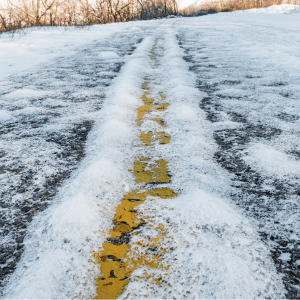Snow-covered road with visible yellow line beneath icy patches.