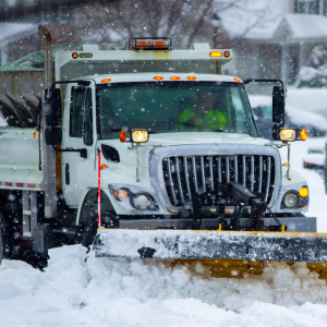 Snowplow clearing heavy snow on a residential street during snowfall.