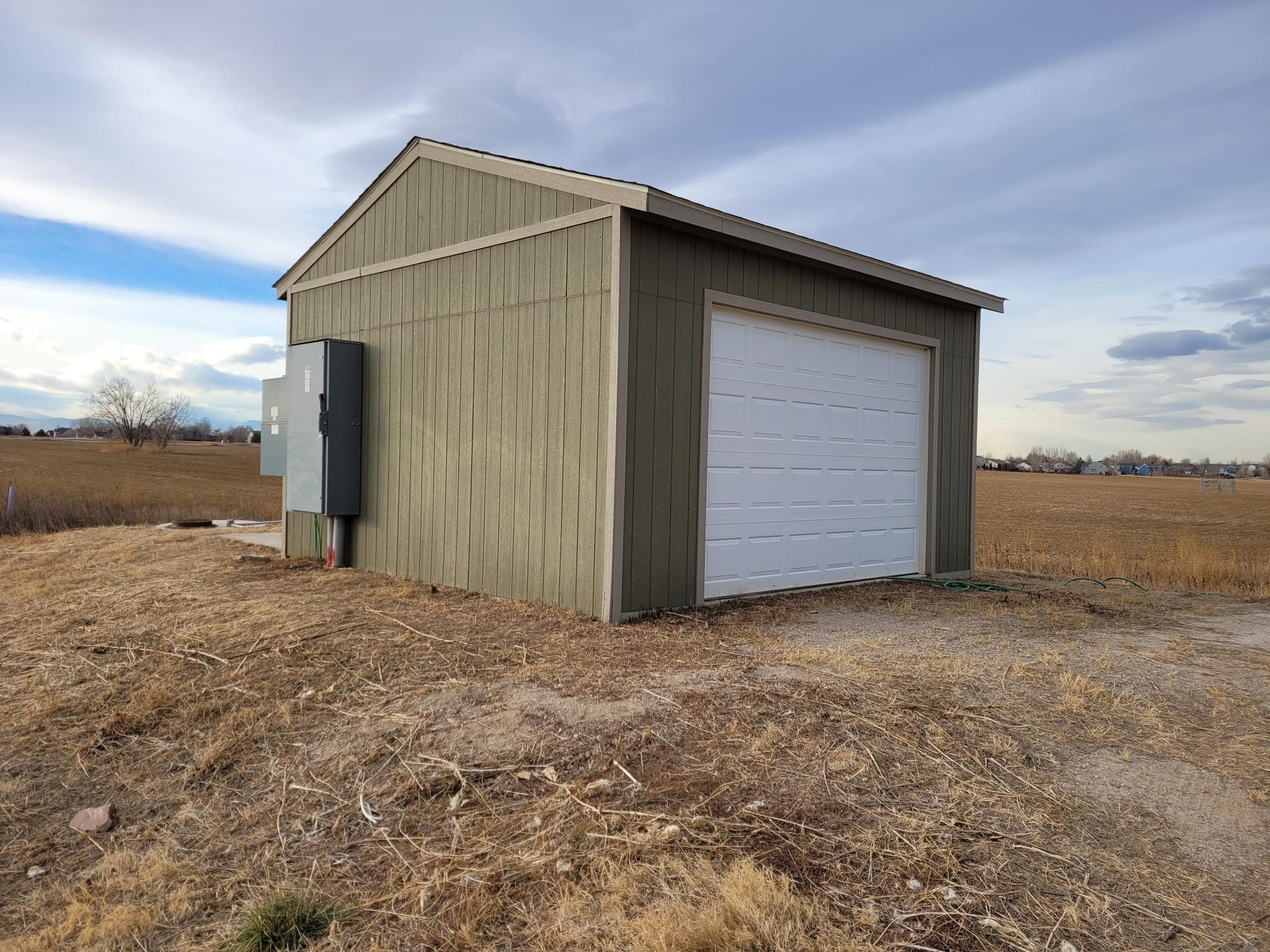 Small green pumphouse with an electrical panel in an open field.