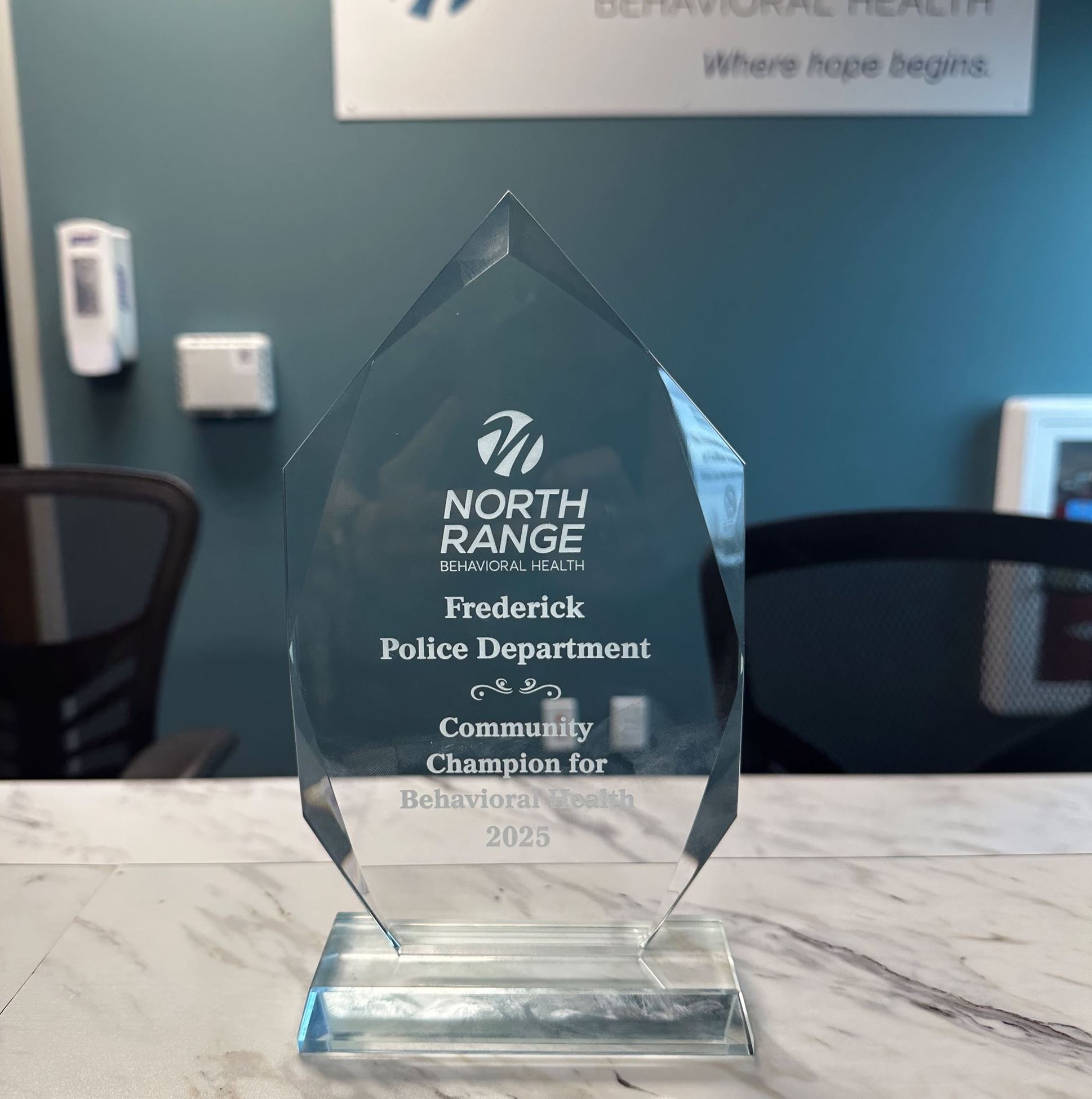 A clear glass award trophy on a marble countertop engraved with “North Range Behavioral Health – Fre