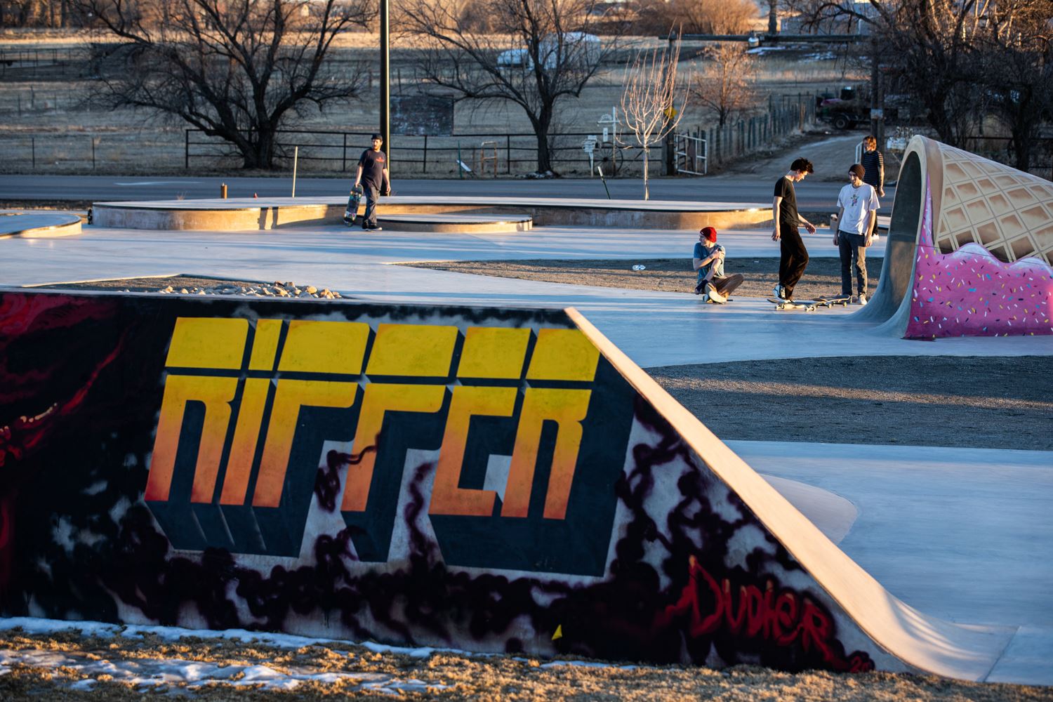 Skatepark scene with several skaters using ramps and obstacles, including a large graffiti ramp